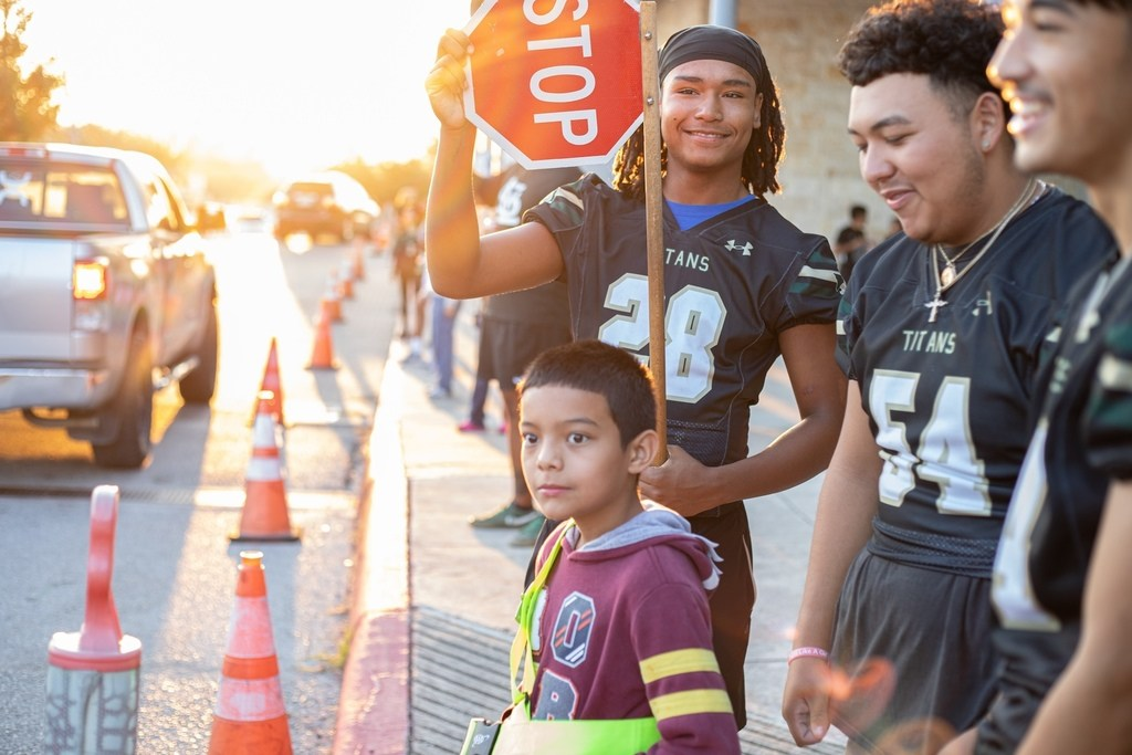 Football players helping elementary student to cross safely