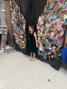 Child Posing in front of artwork made by Wills Point students