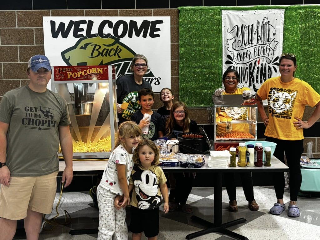 A group children and adults pose near a table with popcorn and hotdog machines on it.