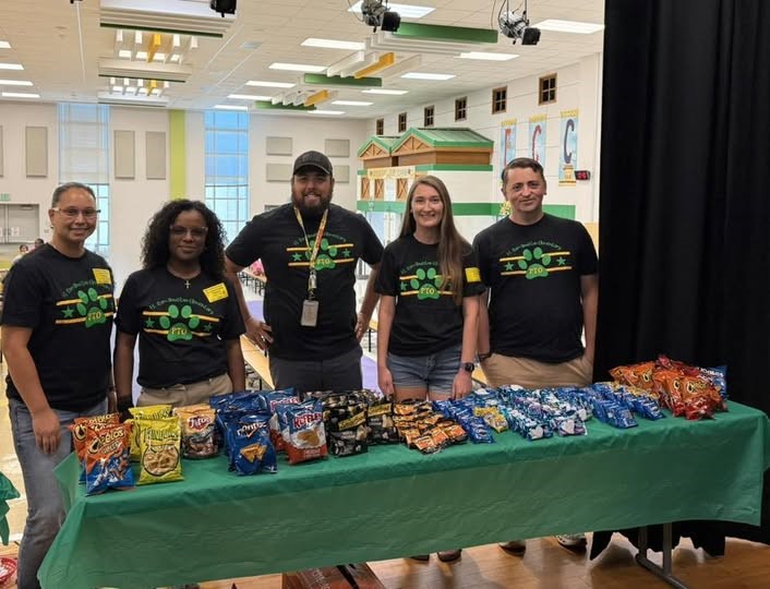 5 volunteers standing behind a table full of snacks.