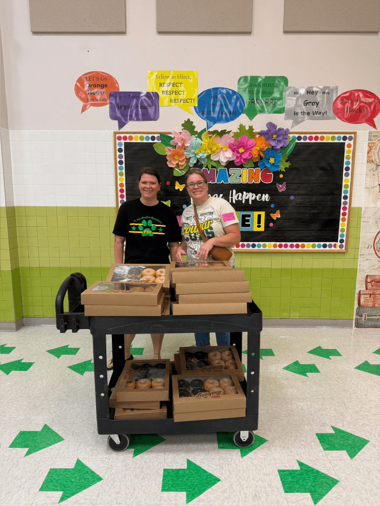 Two volunteers standing behind a cart full of donuts.