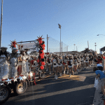 A large group of cheerleaders walking down the street, with some riding on a float.