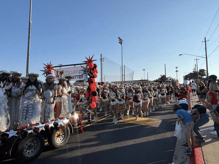 A large group of cheerleaders walking down the street, with some riding on a float.