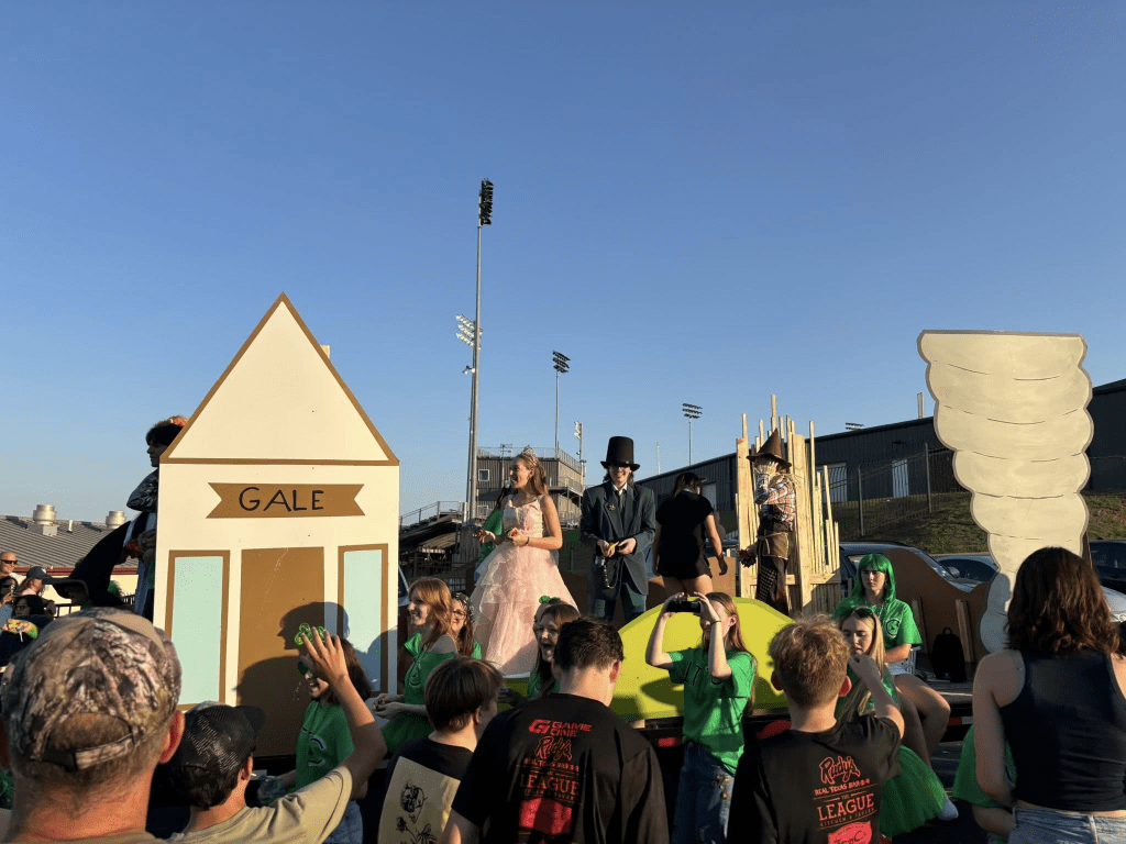 Students stand on a "Wicked"-themed float in front of a crowd.