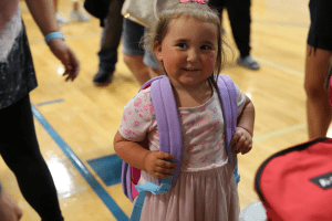 A little girl smiling for a photo, proudly wearing her new backpack.