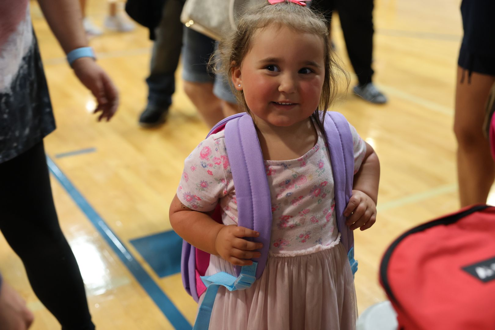 A little girl smiling for a photo, proudly wearing her new backpack.